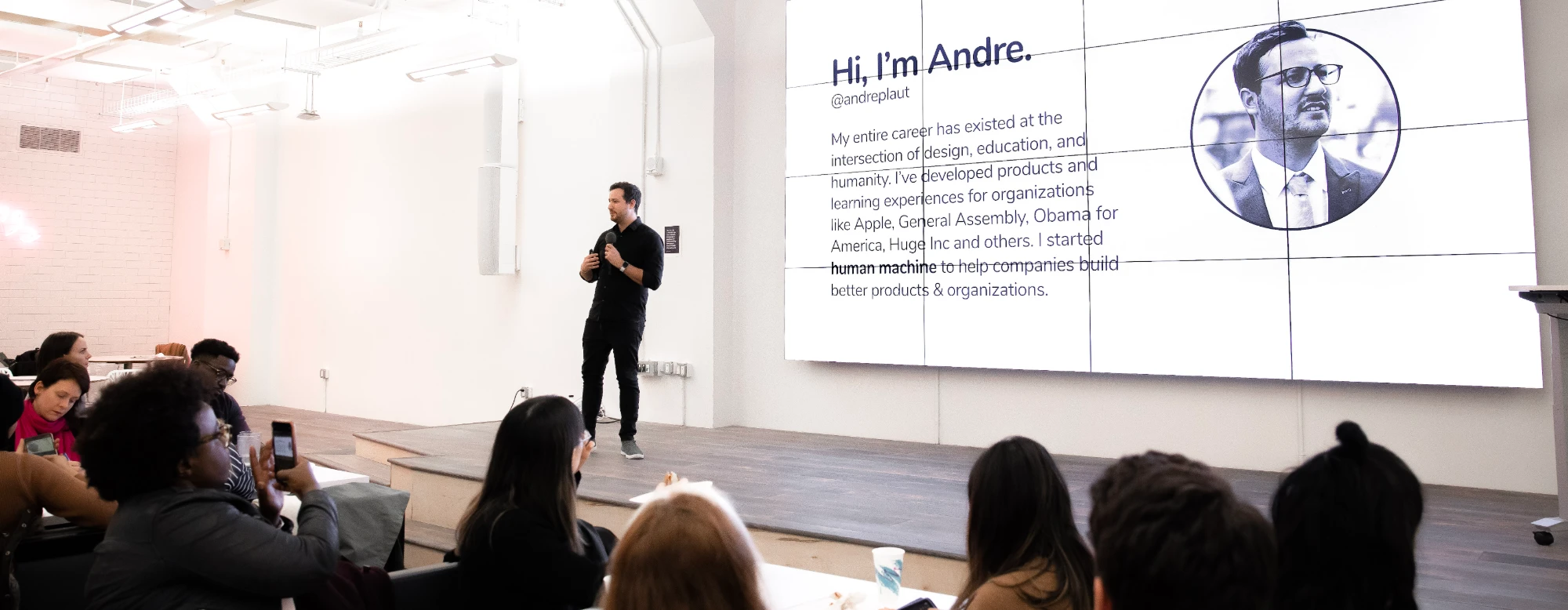 Andre speaking on stage beside a large screen that reads "Hi, I'm Andre."